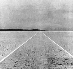 an empty road stretches across the vast expanse of water in this black and white photo