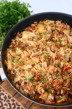 a skillet filled with meat and vegetables on top of a wooden cutting board next to parsley