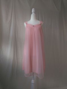 Vintage pastel pink chiffon nightgown. - Sheer overlay against nylon lining - Gorgeous gathered neckline and straps - Dainty embroidered flowers accenting the neckline - A-line silhouette - Straps are not adjustable - Era: Circa 1950s - Condition: Great; There is a slight black mark on the lining. It also seems like the hem was not finished precisely. A small part near the hem was repaired by the previous owner.  - Size: Small - Color: Pastel pink - Brand: Unknown - Measurements: 19in pit to pit, 34in length including straps - Fabric Content: 100% nylon Shown on a mannequin with a 33" bust, 26" waist, and 35" hips. Fits a size 2-4. Some garments may be clipped onto mannequin or model for display. MORE INFO: *Please, note that all items are vintage. Therefore, it is expected to find some we Regency Era Sleepwear, Sheer Coquette Bedtime Dresses, Sheer Sleeveless Coquette Nightgown, Pink Spaghetti Strap Dress For Wedding Night, Pink Sheer Coquette Dress, Pink Sleeveless Slip Dress For Wedding Night, Pink Sheer Camisole Dress, Feminine Sheer Nightgown With Spaghetti Straps, Pink Sheer Dress With Spaghetti Straps