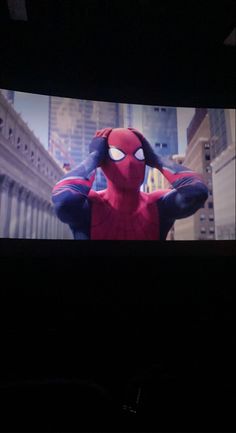 the spider - man is standing in front of a screen with his hands behind his head