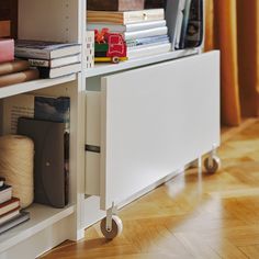 a book shelf filled with lots of books on top of a hard wood floor next to a window