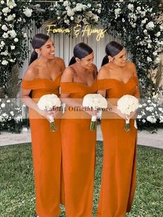 three women in orange dresses standing next to each other with white flowers on the grass