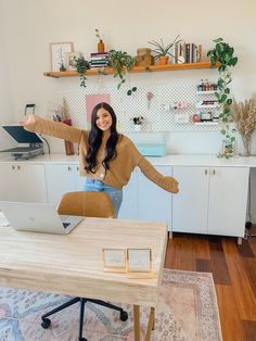 a woman standing in front of a laptop computer on top of a wooden desk next to a plant