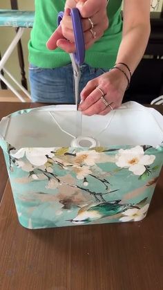 a woman cutting fabric with scissors on top of a table in front of a box