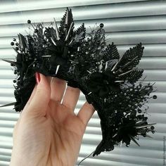 a hand holding up a black hair piece with spikes on it's head and nails sticking out of it