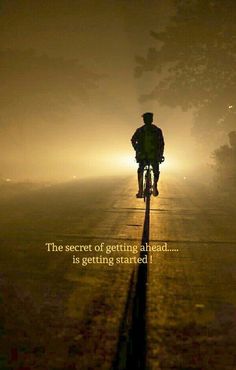 a man riding a bike down a street at night with the sun shining through the fog