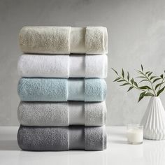 towels stacked on top of each other in front of a white vase with a green plant