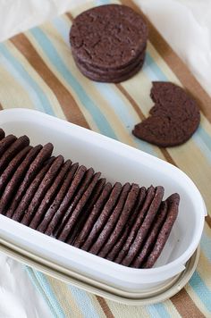 chocolate cookies are in a white dish on a striped tablecloth next to one cookie