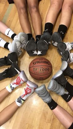 a group of people standing around a basketball on top of a hard wood floor in a circle