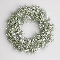 a wreath with white flowers and greenery on the front, hanging from a wall