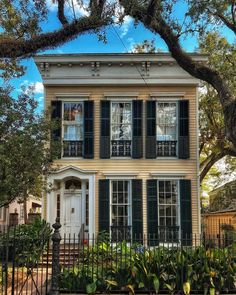 a yellow house with black shutters and trees