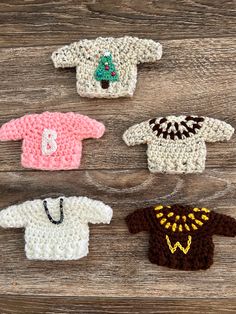 four crocheted baby sweaters sitting on top of a wooden table next to each other