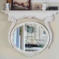 there is a white mirror on the wall above a shelf with pictures and vases