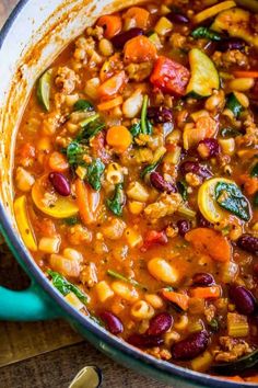 a pot filled with stew and vegetables on top of a wooden table next to a spoon