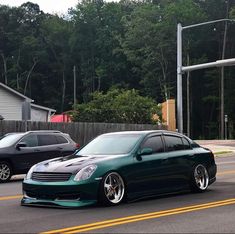 a green car is parked on the side of the road next to two other cars