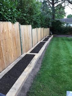 a wooden fence with black soil in the middle and green grass on both sides next to it