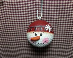 a golf ball ornament with a snowman face on it hanging from a string