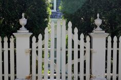 a white picket fence in front of a house with trees on either side and a clock tower behind it