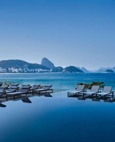 an outdoor swimming pool with chaise lounges facing the ocean and mountains in the background