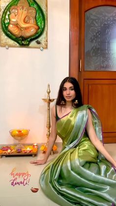 a woman in a green sari sitting on the floor next to a diya