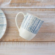 a blue and white cup sitting on top of a wooden table next to a plate