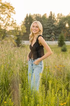 a woman standing in tall grass with her hands on her hips and looking at the camera