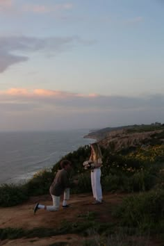 two people standing on top of a hill next to the ocean