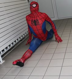 a spider man sitting on the floor in front of a white wall and tiled floor