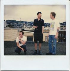 three men standing next to each other on top of a roof with buildings in the background