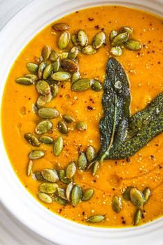 a white bowl filled with carrot soup topped with pumpkin seeds