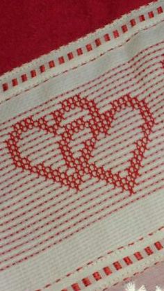 a red and white cross stitched heart on a piece of cloth