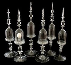 an assortment of glass candlesticks and candle holders, all in different sizes on a black background