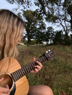 a woman sitting in the grass playing an acoustic guitar