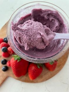 a bowl filled with blueberry ice cream next to strawberries on a cutting board