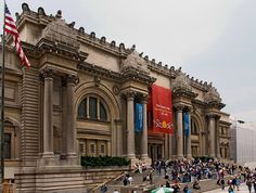 people are walking in front of an old building with columns and flags on the side