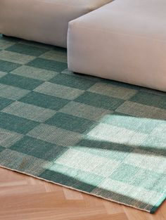 a green and white checkered rug on the floor in front of a couch with pillows