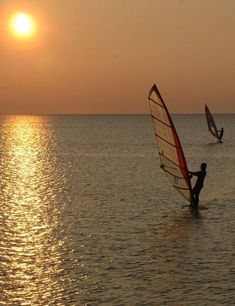 a person windsurfing in the ocean at sunset with another person on board