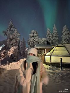 a woman is walking through the snow with an aurora light in the background