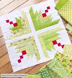 several green and red quilts laid out on a wooden floor with one block cut in half