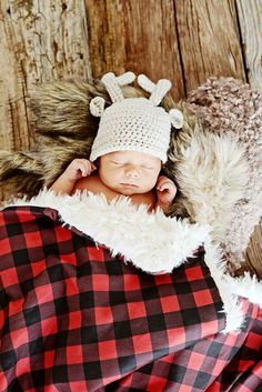 a baby wearing a hat laying on top of a pile of blankets next to a wooden wall