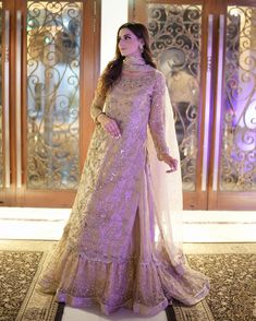 a woman standing in front of a doorway wearing a purple and gold dress with sheer sleeves