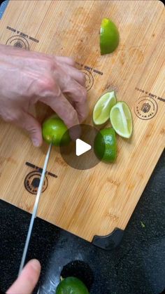 someone cutting limes on a wooden cutting board with a knife and some green peppers