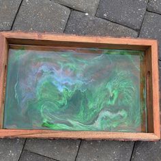 an abstract painting in a wooden frame on the ground next to a brick walkway with cobblestone pavers