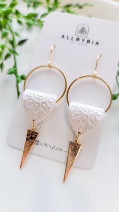 two pairs of earrings with gold and white details on top of a card next to green leaves