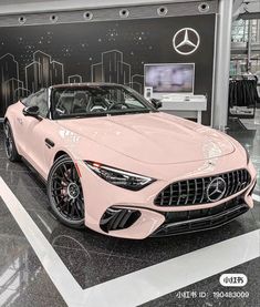 a pink mercedes sports car parked in front of a black and white wall with the mercedes logo on it