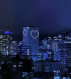 the city skyline is lit up at night with hearts drawn on it's windows