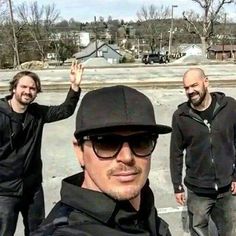 three men standing in a parking lot with one holding his hand up to the sky