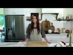 a woman standing in a kitchen next to a counter with a wooden cutting board on it