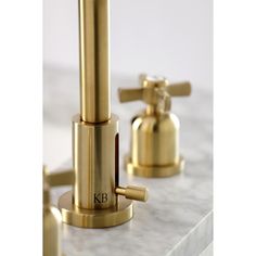 two golden faucets sitting on top of a white marble countertop next to each other