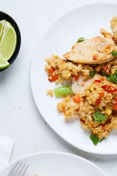 a white plate topped with chicken and rice next to a bowl of lime wedges